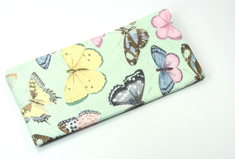 May include: A green fabric eyeglass case with a butterfly print. The butterflies are in various colors, including yellow, pink, blue, and black.