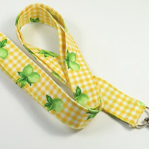 Puede incluir: Lanyard de gingham amarillo y blanco con estampado de limón verde y clip giratorio plateado.