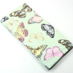 May include: A light green fabric case with a repeating pattern of colorful butterflies. The case is made of a soft, textured fabric.