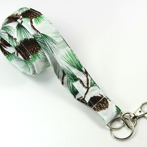 May include: White fabric lanyard with a green and brown pine cone pattern and a silver key ring.