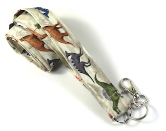 May include: A white fabric lanyard with a dinosaur print and a silver swivel clip. The lanyard is folded in half and the clip is attached to the end.