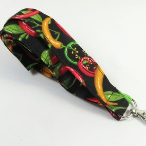 May include: A black fabric lanyard with a red, yellow and green chilli pepper pattern and a silver swivel clip.
