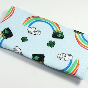 May include: Light blue fabric with a white polka dot pattern. The fabric features a repeating pattern of rainbows, pots of gold, shamrocks, and cartoon dogs.