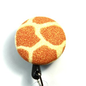 Op de afbeelding: Een ronde, gele en oranje intrekbare badgehouder met een giraffenprint.