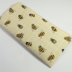 May include: A beige fabric pencil case with a repeating pattern of cartoon bees wearing hats and carrying buckets. The bees are yellow and black with brown eyes and green hats.