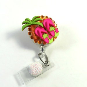 May include: A pink and green flip flop charm with a palm tree and orange rhinestones on a clear retractable badge holder with a white glitter seashell.