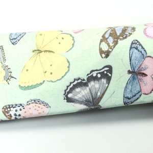 May include: A green fabric eyeglasses case with a butterfly print. The case is closed and has a brown pair of glasses inside.