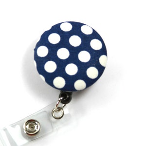 Puede incluir: Un portagafete retráctil de lunares azules y blancos con una correa de plástico transparente.