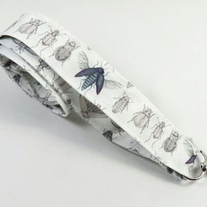 May include: White fabric lanyard with a silver key chain. The lanyard is printed with a pattern of various insects, including beetles and butterflies.