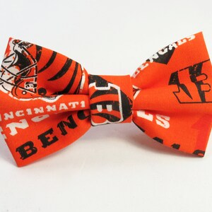 May include: Orange bow tie with a white and black print of the Cincinnati Bengals logo and the words "Cincinnati Bengals".