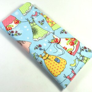 May include: A blue fabric with a repeating pattern of colorful dresses hanging on a clothesline. The dresses are decorated with polka dots, flowers, and other patterns. There are also small birds and flowers on the fabric.