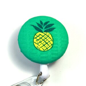 May include: A green fabric badge reel with a yellow pineapple design. The reel is attached to a white retractable cord.