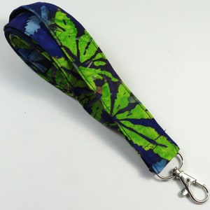 Puede incluir: Un cordón de tela azul y verde con un cierre giratorio plateado. La tela tiene un patrón batik con hojas verdes sobre un fondo azul.