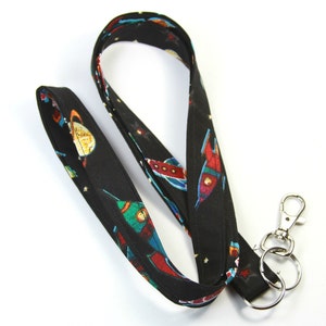 May include: A black lanyard with a space-themed print featuring rockets and planets. The lanyard has a silver swivel clip and a silver key ring.