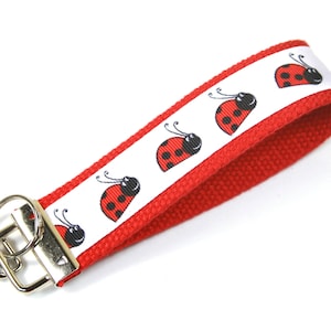May include: Red and white key chain with a silver key ring and a repeating pattern of ladybirds.