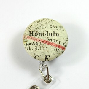 May include: A beige fabric badge holder with a map of Honolulu, Hawaii. The map features the text "Honolulu", "Hawaii (U.S.)", "San Fran 2098 Miles", "Cancer", "Short Route", and "Via P".