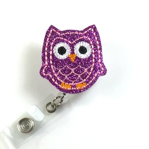 Può includere: Portachiavi con rotolo per badge a forma di gufo con glitter viola, cuciture rosa e piedi arancioni. Il gufo ha occhi bianchi con pupille nere.