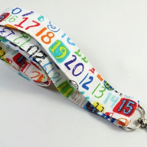 May include: White fabric lanyard with a colorful print of numbers 1 through 15. The lanyard has a silver metal clip.