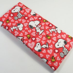 Può includere: Custodia per occhiali in tessuto rosso con un motivo ripetuto di Snoopy che tiene un cuore e un piccolo uccellino giallo.