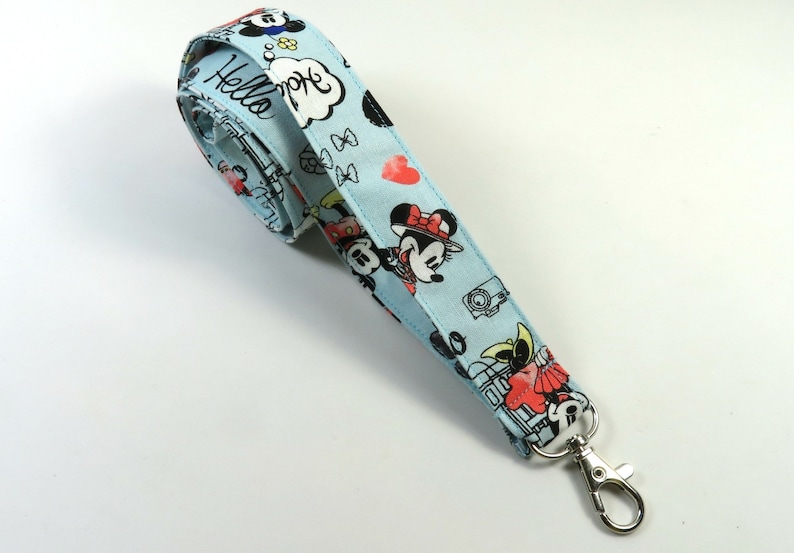 May include: A light blue lanyard with a Mickey Mouse and Minnie Mouse print. The lanyard has a silver metal clip. The lanyard has the text "Hello" and a speech bubble with the text "Hope" on it.