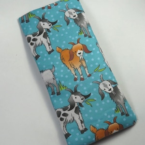 May include: A rectangular piece of fabric featuring a repeating pattern of cartoon goats in shades of white, grey, and orange on a bright turquoise background with white polka dots and small green grass patches.