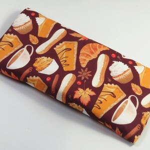 Puede incluir: Una tela marrón con un patrón repetido de golosinas de otoño, que incluyen pastel de calabaza, cupcakes, croissants y café. La tela es perfecta para proyectos de manualidades como almohadas, bolsos y otros artículos de decoración del hogar.