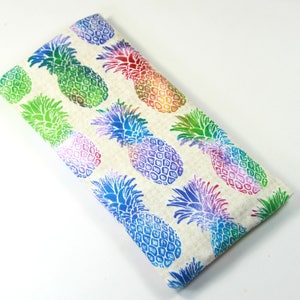 May include: A beige fabric eyeglass case with a repeating pattern of rainbow colored pineapples.