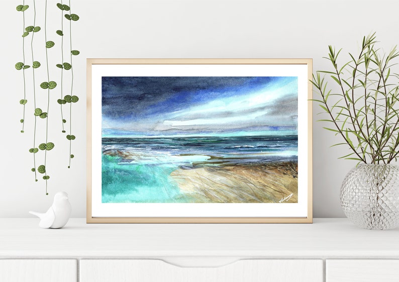 May include: A watercolor painting of a seascape with a stormy sky and turquoise water. The painting is framed in a light wood frame.