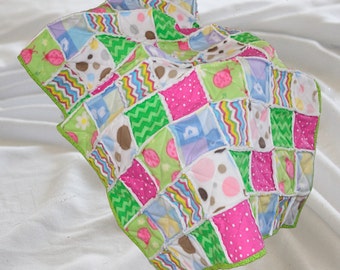 Könnte beinhalten: Eine Patchwork-Babydecke mit einer Vielzahl von bunten Stoffen, darunter rosa, grün, blau und weiß. Die Decke besteht aus Quadraten mit verschiedenen Mustern, darunter Punkte, Streifen und Blumen. Die Decke ist mit einem grünen Besatz eingefasst.