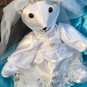 K&ouml;nnte beinhalten: Wei&szlig;er Satin-Teddyb&auml;r, der ein wei&szlig;es Brautkleid mit Schleier, Spitzenbesatz und Perlenverzierungen tr&auml;gt.