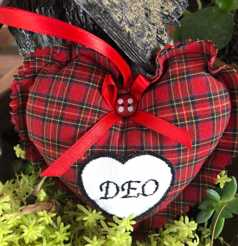 May include: Red and black plaid heart-shaped pillow with a white heart embroidered with the word "DEO" and a red button with white dots in the center.
