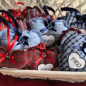 May include: A basket filled with handmade heart-shaped pillows. The pillows are made of blue and red plaid fabric and have white embroidered lettering that says "DEO".