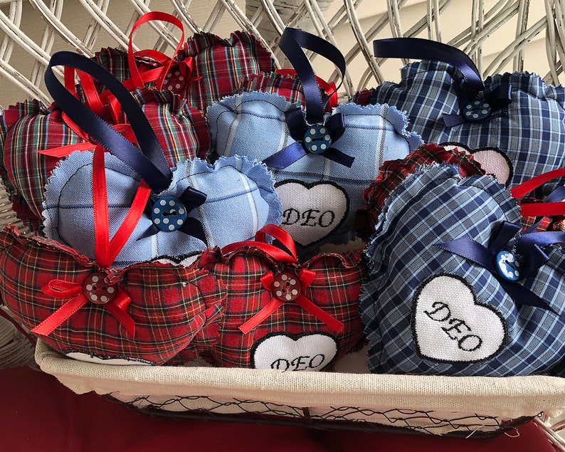 May include: A basket filled with handmade heart-shaped pillows. The pillows are made of blue and red plaid fabric and have white embroidered lettering that says "DEO".