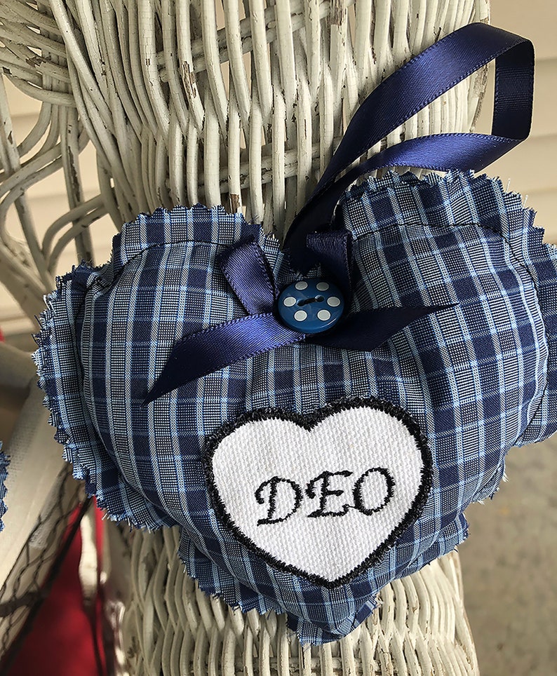 May include: Blue and white plaid heart-shaped pillow with a white heart-shaped patch that says "DEO" in black embroidery. The pillow has a blue ribbon and a blue button with white dots.