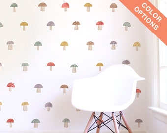 May include: A white wall with a variety of colorful mushroom stickers. The mushrooms are in different patterns and colors, including red, yellow, green, and purple. The stickers are arranged in a random pattern on the wall. A white chair with wooden legs is in the foreground.