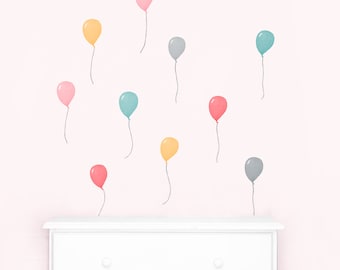 May include: A set of pastel colored balloon wall decals. The decals are in shades of pink, yellow, blue, and gray. The balloons are floating on a white wall.