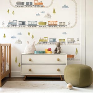 May include: A child's room with a white chest of drawers, a cot, and a green footstool. The wall has a watercolour train and track design, with trees and clouds. Toys and a soft toy sit on the drawers. The room has a neutral colour scheme.