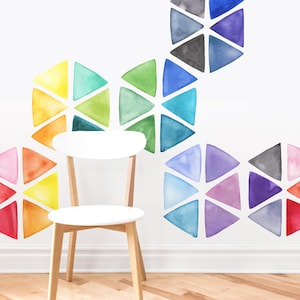 Puede incluir: Una silla blanca se encuentra frente a una pared con un patrón geométrico colorido. El patrón está formado por triángulos de acuarela en tonos de rojo, naranja, amarillo, verde, azul, morado y gris. Los triángulos están dispuestos en un patrón repetitivo de hexágonos.