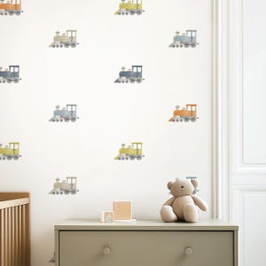 May include: A white wall adorned with watercolor train decals in various colors, including yellow, blue, and orange. A neutral-toned dresser with a teddy bear and wooden blocks sits below the decals, creating a playful nursery theme.