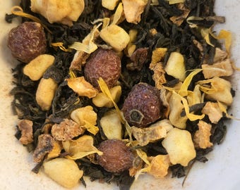 May include: A close-up of a white bowl filled with a blend of loose leaf tea. The tea includes black tea leaves, dried orange peel, and dried rose hips.