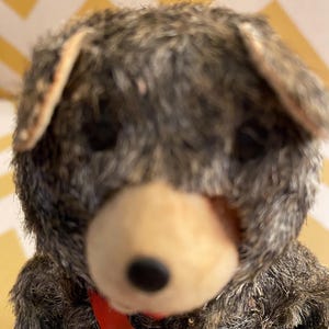 May include: A vintage plush toy bear with brown fur, a black nose, and a red scarf. The bear is wearing a brown vest and has a worn, vintage look.