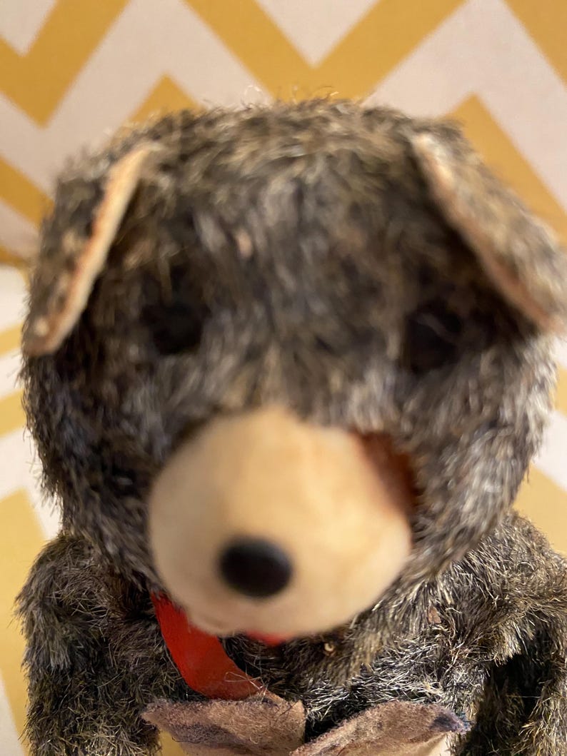May include: A vintage plush toy bear with brown fur, a black nose, and a red scarf. The bear is wearing a brown vest and has a worn, vintage look.