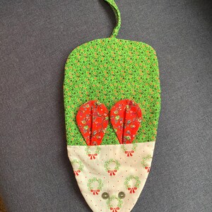 May include: A green and red fabric mouse-shaped stocking with a white fabric bottom featuring a wreath pattern. The stocking has a loop at the top for hanging.