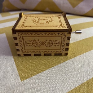 May include: A wooden music box with a hand-crank on the side. The top of the box has a decorative design with the word "love" in the center.