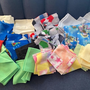 May include: A collection of colorful fabric squares, including red, blue, green, yellow, and white. The squares are made of fleece and have various patterns, including stars, stripes, and geometric designs.