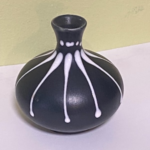 May include: A small, dark blue ceramic vase with white abstract lines. The vase has a rounded body and a narrow neck.