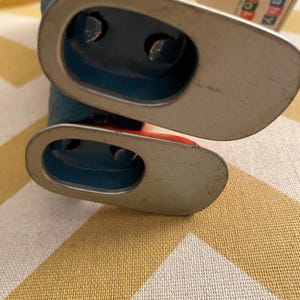 May include: A vintage tin toy robot with blue and red paint. The robot has a silver base and is missing one arm. The robot is on a yellow and white checkered surface.