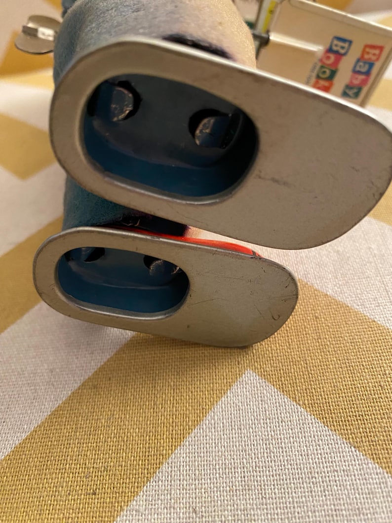 May include: A vintage tin toy robot with blue and red paint. The robot has a silver base and is missing one arm. The robot is on a yellow and white checkered surface.