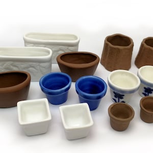 Könnte beinhalten: Eine Sammlung von 12 kleinen Keramik-Töpfen in verschiedenen Farben und Stilen, darunter weiß, braun, blau und weiß mit blauen Blumenmustern. Die Töpfe sind auf einer weißen Oberfläche angeordnet.