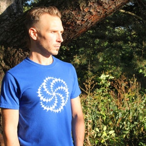 Puede incluir: Un hombre lleva una camiseta azul real con un dise&ntilde;o geom&eacute;trico blanco. El dise&ntilde;o es un patr&oacute;n circular de puntos y l&iacute;neas blancas.